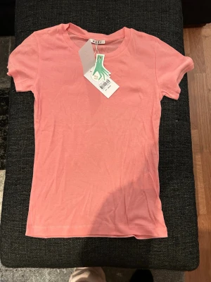 Rosa t-shirt från WERA XS - Snygg rosa t-shirt från WERA i storlek XS. Klassisk rund halsringning och korta ärmar. Tillverkad i mjuk bomull som känns skön mot huden. Enkel och stilren design som passar till allt.