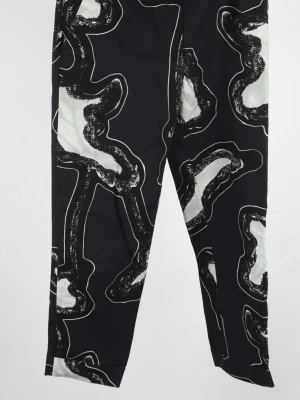 Svarta mönstrade byxor från COS - Unika svarta byxor från COS med abstrakt vitt och svart mönster. Tillverkade i mjuk bomull med lite stretch för extra komfort. Raka ben och normal passform, perfekta för dig som vill sticka ut med din stil.