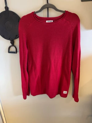 Röd stickad tröja Jack & Jones S - Säljer en röd stickad tröja från Jack & Jones Originals i storlek S. Tröjan har rund halsringning, lång ärm och en enkel, clean design med liten logolapp nertill. Perfekt för lager-på-lager under höst och vinter.