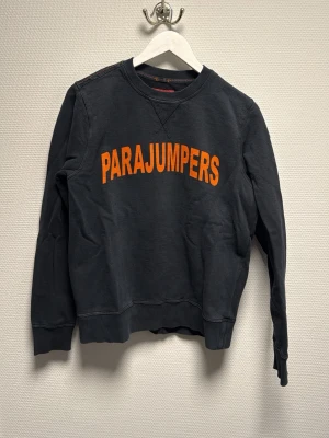 Svart tröja Parajumpers  - Svart fleece-tröja från Parajumpers med orange logga framtill och patch på ärmen. Klassisk rund hals, ribbade muddar och kontrastsömmar. Perfekt för kyliga dagar och riktigt skön att ha på sig. Skriv för frågor
