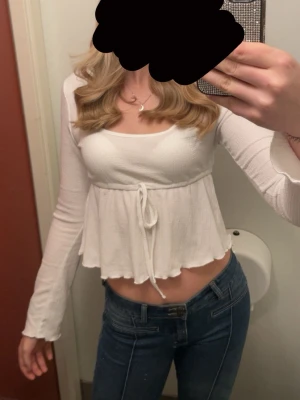 Vit croppad blus med knyt - Säljer en söt vit croppad blus med långa ärmar och knyt i midjan. Toppen har en lätt rynkad struktur och volangkant nedtill. 