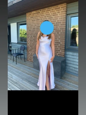 Ljuslila långklänning med slits - Säljer min  ljuslila balklänning i glansigt material med smala axelband och snygg slits framtill. Ryggen är öppen. Klänningen har en draperad urringning och figurnära passform som ger en riktigt snygg siluett. Perfekt för student eller bal!🩷Jag är 170 och bär storlek 36