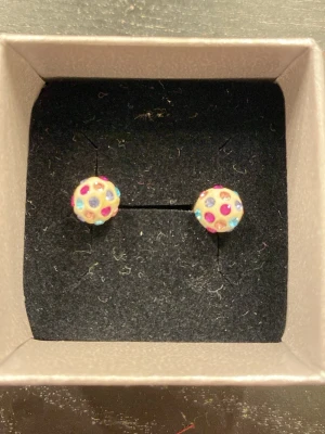 Färgglada prickiga örhängen - Säljer ett par runda örhängen med vit bas och färgglada prickar i rosa, blått, lila. Perfekta för att ge din look lite extra färg och lekfullhet.