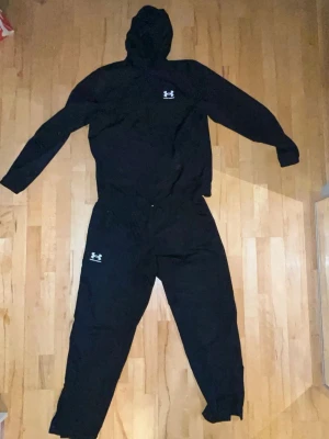 Svart Under Armour träningsset  - Säljer ett träningsset från UA pga byte av klädstil, byxorna är i storlek XL (men passar dig som har L) och jackan M