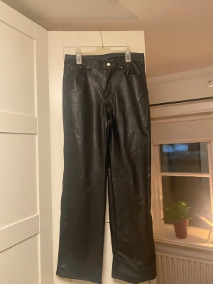 Svarta raka byxor i fejkskinn H&M - Säljer ett par svarta byxor i fejkskinn från H&M, storlek 42. Byxorna har raka ben och normal midja. Materialet är mjukt och insidan är fodrad för extra komfort. Perfekta till vardags. (Sömmen längst ner på ena benet har gått sönder lite)
