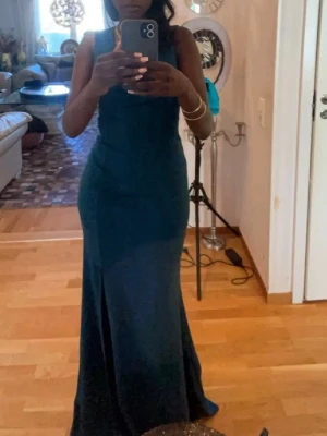 Mörkgrön långklänning med slits - Säljer en elegant mörkgrön långklänning med v-ringning och ärmlös design. Använd 2 gånger men precis som ny. Nypris: 2500kr. Klänningen har en figurnära passform och en snygg slits framtill som ger extra edge. Perfekt för dig som vill sticka ut med en stilren look. Materialet känns mjukt och följsamt mot kroppen.