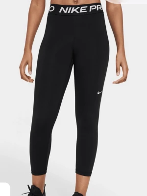 Svarta Nike Pro leggings - Svarta Nike Pro leggings med hög midja och tydlig logga i midjebandet. Tight passform och croppad längd, perfekta för träning. Tillverkade i stretchigt syntetmaterial som andas.