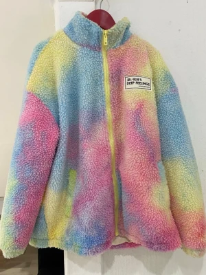 Färgglad teddyjacka Deep Feelings - Säljer en fluffig teddyjacka med regnbågsfärgade toner i blått, rosa, gult och lila. Jackan har hög krage, gul dragkedja och ett patch med texten 'Deep Feelings' på bröstet. Perfekt för dig som gillar mjuka och färgstarka plagg.