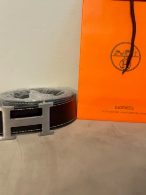 Svart med silver logga - Stilrent svart bälte med silver logga, 110cm