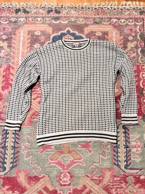 Fiske tröja från Northbrook - Säljer en vit och svart stickad fiske tröja från Northbrook med ett tätt, grafiskt mönster. Tröjan har rund hals, ribbade muddar och nederkant med svarta ränder. Perfekt för dig som gillar retrovibbar och vill ha något unikt i garderoben.