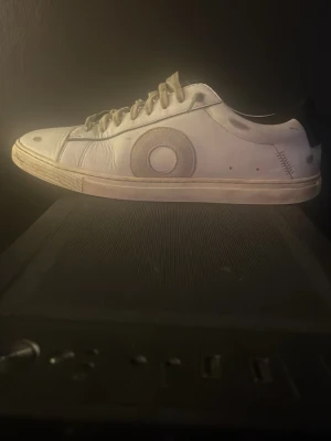 Oliver Cabell vita sneakers strl 39 - Säljer ett par vita sneakers från Oliver Cabell i storlek 39. Skorna har ett unikt cirkelmönster på sidorna. Tillverkade i skinn och levereras med originalkartong och dustbag. Perfekt för dig som gillar stilrena och coola detaljer. Gjorda i Italien och nypris 3050kr!