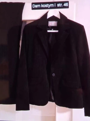 Svart manchesterkostym dam strl 46 - Säljer en svart damkostym från Vera i storlek 46. Kostymen består av en klassisk kavaj med krage och knapp framtill samt matchande byxor. Materialet är mjuk manchester som ger en cool och tidlös känsla. Perfekt för dig som gillar stilrena och bekväma plagg.