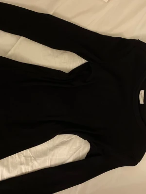 Svart ribbad långärmad topp XS - En svart, ribbad långärmad topp från Gina Tricot i storlek XS. Toppen har rund hals och är figurnära i modellen, perfekt att styla med jeans eller kjol. Materialet är mjukt och stretchigt för en bekväm passform.