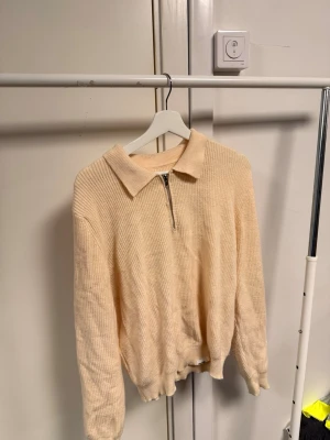 Beige stickad tröja med krage och zip - Snygg beige stickad tröja med klassisk krage och half zip framtill. Tröjan har långärmade ribbade ärmar och en mjuk, lite loose passform. Perfekt för dig som gillar stilrena och bekväma plagg med en enkel twist.