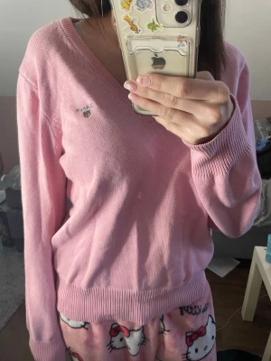 Rosa stickad v-ringad tröja GANT - Säljer en ljusrosa stickad tröja från GANT med v-ringning och broderad logga på bröstet. Tröjan har långa ärmar och ribbade muddar vid hals, ärmslut och nederkant. Perfekt för dig som gillar klassisk och chill stil.💕