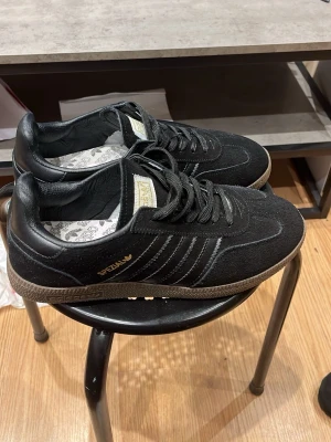 Adidas Spezial svarta sneakers - Adidas Spezial sneakers i svart mocka och skinn med klassiska tre ränder på sidan och guldtext. Snygg gummisula i beige ton och snörning framtill. Insidan har Adidas-logga på innersulan. Perfekt för dig som gillar retrostil och streetwear . Passar 40/41/42 