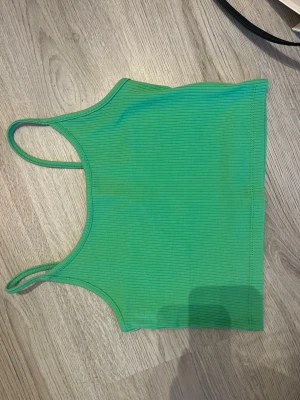 Grön ribbad croppad linnetopp - Säljer ett grön croppad linne med smala axelband och ribbad struktur. Toppen har en enkel och stilren design och är perfekt för varma dagar. Materialet känns mjukt och stretchigt mot huden.