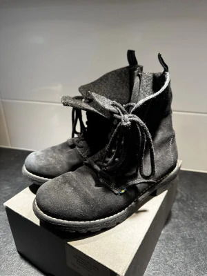 Svarta mockaboots från Kavat stl 34 - Säljer ett par svarta boots från Kavat i storlek 34. Skorna är i mocka med snörning framtill, dragkedja på sidan och grov sula för extra grepp. Insidan är fodrad med grå filt för värme och komfort. Perfekta för kyligare dagar.