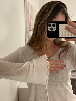 Vit långärmad blus från Nelly - Supersöt vit blus från Nelly i tunn och lätt bomull. Den har v-ringning, långa ärmar med volangkant och vågig nederkant. Perfekt att styla med jeans eller kjol för en fräsch look. Storlek XS.