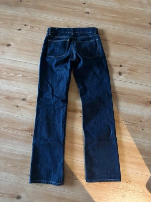 Mörkblå raka jeans - Säljer ett par mörkblå jeans med raka ben och klassisk femficksdesign. Jeansen har kontrastsömmar och är tillverkade i robust denim. Perfekta för dig som gillar en enkel och tidlös look.