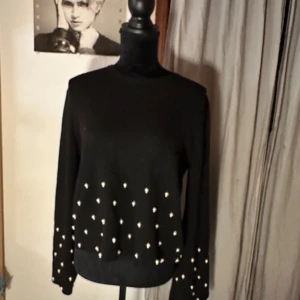 Svart tröja med pärlor från H&M - Svart långärmad tröja från H&M i storlek S. Tröjan är dekorerad med pärlor på både framstycket och ärmarna, vilket ger en snygg och trendig look. Perfekt att styla med jeans eller kjol för en cool outfit.