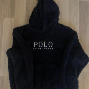 hoodie Polo Ralph Lauren - Mysig mörkblå hoodie från Polo Ralph Lauren i fluffig fleece med stor broderad logga på bröstet och klassisk polo logga på vänstra ärmen. Tröjan har huva och en loose passform som är perfekt för chill dagar. Snyggt och stilrent märke för dig som gillar street och premium.