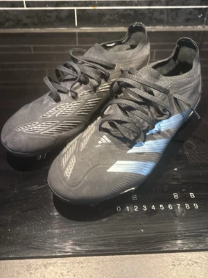 Adidas Predator svarta fotbollsskor - Säljer ett par svarta Adidas Predator fotbollsskor med snörning och mönstrade detaljer i silver och grått. Skorna har rund tå, platt sula med dobbar och är tillverkade i syntetmaterial. Perfekta för dig som vill ha grym kontroll på planen. Oanvända. Nypris ligger på 1699 kr. Pris kan diskuteras 
