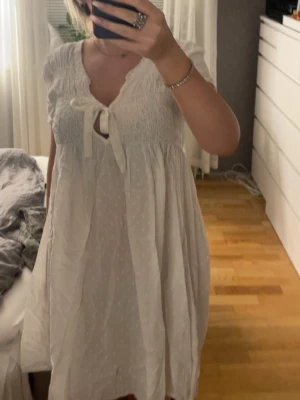 vit Odd Molly kortklänning med knyt - supersöt vit kortklänning från Odd Molly, modell twenty-four-seven dress. klänningen har korta puffärmar, smock upptill och ett fint knyt vid halsen. materialet är bomull med diskret prickigt mönster och volangkant vid halsen. perfekt för sommaren!finns ingen storlek men skulle gissa på en M. 