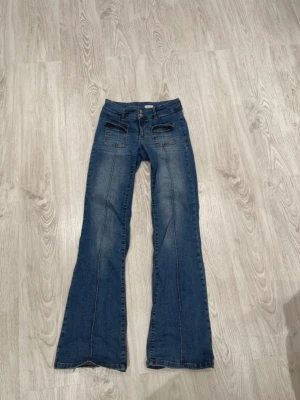 Blå bootcut jeans med fickor - Säljer ett par blå bootcut jeans med markerade sömmar och två stora fickor framtill. Jeansen har klassisk knapp- och dragkedjestängning och är tillverkade i ett mjukt denimtyg. Perfekta för dig som gillar retrovibbar och vill ha en snygg siluett.