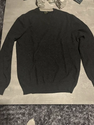 Mörkgrå kashmirtröja Massimo Dutti - Säljer en stilren mörkgrå tröja från Massimo Dutti i mjuk kashmir. Klassisk v-ringad modell med långa ärmar och ribbade muddar. Perfekt för dig som gillar en clean och tidlös look.