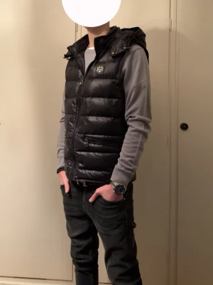 Svart dunväst från Bvaldi med huva - Säljer en svart dunväst från Bvaldi i storlek M. Västen har en quiltad design, dragkedja framtill, två fickor med dragkedja och en stor huva. Som är enkel att ta av om man vill. Materialet är 100% polyamid och den har en stilren look med Bvaldi-logga på bröstet. Perfekt för lager-på-lager under kyliga dagar. Och nypris ligger på 1800. Jag har även bara använt den någon gång för de blev sedan för kallt. Västen är alltså i toppen skick och har inga defekter skriv om du har några frågor.