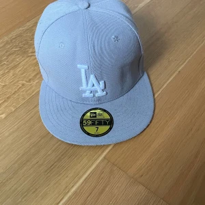 Ljusgrå LA Dodgers keps New Era 59FIFTY - Snygg ljusgrå LA Dodgers keps från New Era, modell 59FIFTY. Kepsen har broderad LA-logga framtill, World Series 1988-brodyr på sidan och New Era-logga. Rak skärm och klassisk passform. Perfekt för dig som gillar streetwear och sportig stil.