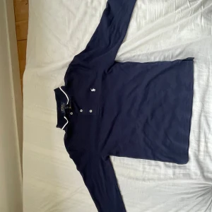 Marinblå långärmad Polo Ralph Lauren pikétröja i ull  - Jätte bekväm långärmad marinblå polo Ralph lauren piké i ull. L (14-16) barn storlek. Super bra skick, inga defekter och bara använd ungefär 5 gånger. Link till tröjan för mer info https://www.ralphlauren.eu/se/en/dpid-authenticated?authActionId=VmwAUfKdTqwCmTfPBMVnBmGt&webstoreAvailable=true Kontakta gärna vid frågor🤗!