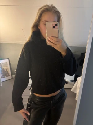Svart croppad hoodie med huva - Svart croppad hoodie med huva och långa ärmar. Tröjan har en loose passform och är enkel i designen utan synliga detaljer eller mönster. Perfekt för dig som gillar en avslappnad och stilren look.