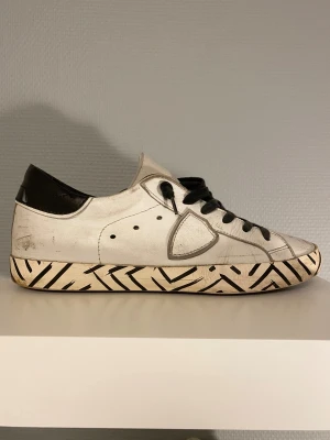 Philippe Model skor - Säljer dessa vita Philippe Model skorna med svarta detaljer på sulan. Skorna kommer i stl 40 och är i hyfsat bra skick, de mesta slitningarna är design. Undersulan är dock lagad med lim eftersom den brast lite vid hälen. Hör av er vid frågor!