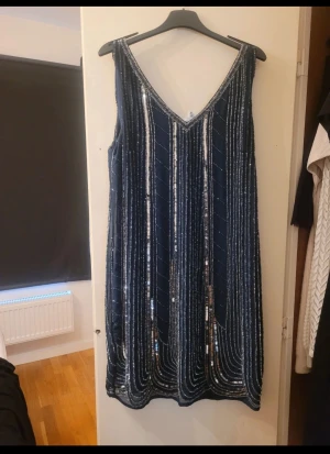 Marinblå paljettklänning från Maya - Säljer en marinblå klänning från Maya Tall med glittriga paljetter i vertikala rader. Klänningen har v-ringad hals och är ärmlös, vilket ger en snygg och festlig look. 