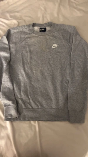 Grå hoodie/Sweatshirt - Säljer en Nike sweatshirt-hoodie i acceptabelt skick. Den har en fläck mitt på framsidan, men annars är den i bra form och materialet har hållit sig fint. Tyget är lite tunnare, vilket gör den perfekt för både lager på lager, träning och vardag. Designen är stilren och lätt att styla  funkar till allt och passar både herr och dam (unisex)