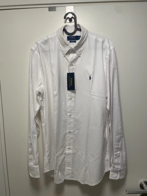 Vit skjorta från Polo Ralph Lauren - Klassisk vit skjorta från Polo Ralph Lauren med button-down krage och blå broderad logga på bröstet. Helt ny, med tags! Passade inte mig därför säljs.