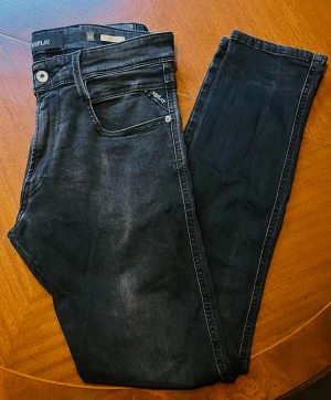 Replay Anbass svarta jeans, storlek 32 - Svarta jeans från Replay, modell Anbass, med klassisk femficksdesign och diskret Replay-logga på fickan. Jeansen har en smal passform och är tillverkade i stretchigt denim för extra komfort. Perfekt för dig som gillar stilrena och moderna jeans. Nypris: 2199kr