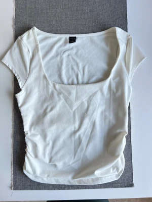 Vit croppad topp - Säljer en vit croppad topp med fyrkantig ringning och korta ärmar. Toppen har  rouched detaljer i sidorna som accentuerar midjan snyggt 🤍 Knappt använd, bra kvalitet