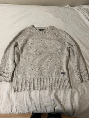 Beige stickad tröja Peak Performance - Säljer en beige stickad tröja från Peak Performance i storlek S. Tröjan har ett diskret melerat mönster, rund hals och breda ribbade muddar vid ärmslut och nederkant. Perfekt för kyliga dagar och har en klassisk, chill vibe.  Ops! ⚠️ står s men passar till 10-11 åringar 