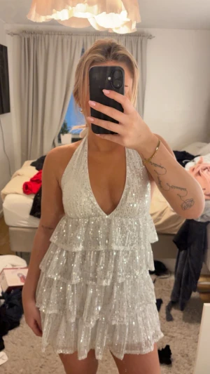 Glittrig vit kortklänning med volanger - Superfin glittrig klänning, med öppen rygg. Har sytt dit bh inlägg så man inte ser igenom klänningen och kan ha på sig den utan bh och tejp. (Går enkelt att klippa bort om man så vill det). Köpt för 300kr på Plick. 
