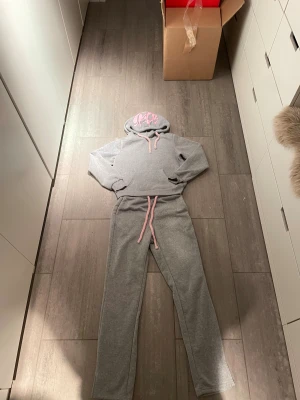 Grå/rosa tracksuit - Säljer en sjukt snygg och trendig track suit. Storlek XS på både byxorna och hoodien. HELT NYTT SKICK! Aldrig en använd. 10/10 skick. Säljer som sett för 599kr kontakta vid minsta intresse!