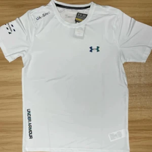 Vit Under Armour t-shirt HeatGear - Snygg vit t-shirt från Under Armour med svart logga på bröstet och tryck på ärm och nederkant. Tillverkad i lätt och ventilerande polyester med HeatGear-teknologi, perfekt för träning. Klassisk rund hals och korta ärmar för en sportig look.