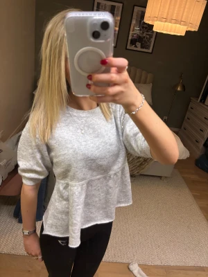 Grå peplumtröja från Nelly XS - Superfin ljusgrå stickad tröja från Nelly i peplum-modell med rund hals och puffiga trekvartsärmar. Mjuk och skön, perfekt för dig som gillar en söt och chill stil. Passar dig som vill ha något som sticker ut lite med volangdetalj nedtill.