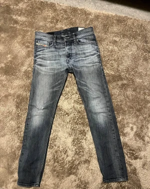 Diesel Tepphar slim jeans grå W28 L30 - Snygga Diesel Tepphar slim jeans i grå tvätt med coola slitningar och klassisk femficksdesign. Stretchigt material för skön passform och smal siluett. Perfekt för dig som gillar en modern och stilren look. Diesel Industry-detalj på fickan.