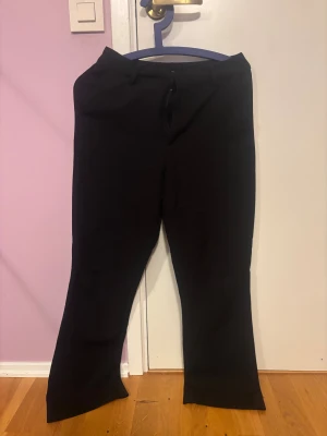 Svarta kostymbyxor med bootcut - Snygga svarta kostymbyxor med bootcut-snitt och klassisk midja. Byxorna har bälteshällor och en stilren look som passar till många olika outfits. Materialet känns mjukt och har en lätt stretch för extra komfort. modell VILMA från bikbok