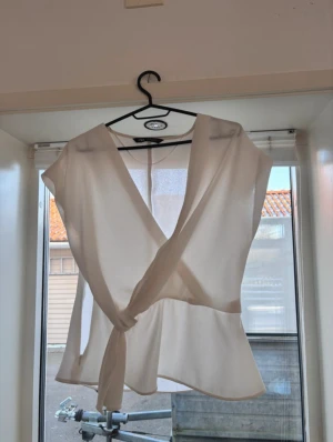 Vit omlottopp från Zara - Säljer en vit blus från Zara i storlek S. Toppen har korta ärmar, v-ringad hals och knyt i midjan som gör att blusen sitter fint. Materialet är lätt och luftigt. 
