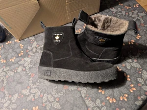 Svarta boots från Canada Snow - Svarta boots från Canada Snow i mocka med grov sula och mjukt, brunt foder inuti. Skorna har dragkedja på sidan och praktiska öglor för enkel påtagning. Perfekta för kalla dagar när du vill hålla stilen och värmen. Använda enstaka gång 