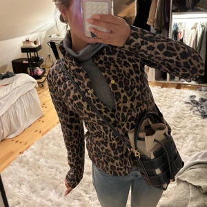 Leopardmönstrad pufferjacka - Säljer en snygg pufferjacka med leopardmönster och guldiga knappar. Jackan har figurnära passform, hög krage och långa ärmar. Perfekt statement-plagg för dig som vill sticka ut. Färgerna går i beige och brunt med svarta detaljer.